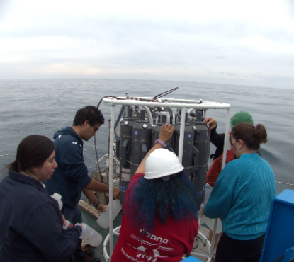 Students gathered around a rosette water sampler on the deck of a research vessel