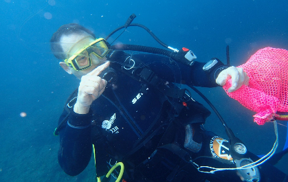 Diver in full gear underwater holding a pink collection mesh bag