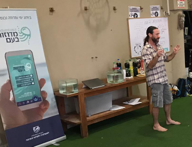 A researcher presenting the Meduzot Ba'am project at a diving club, beside a project banner and small aquariums