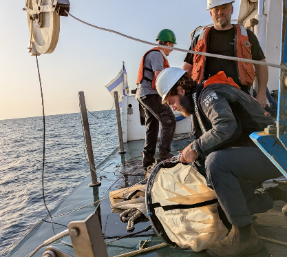 Crew and students handling a plankton net on deck at sunrise