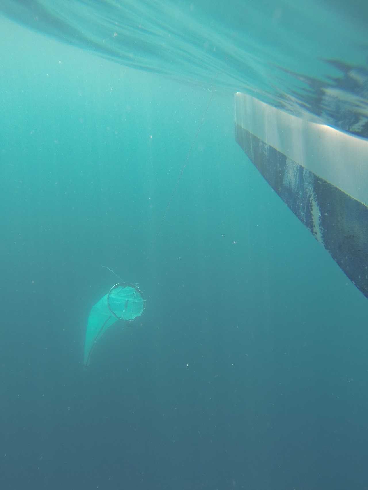 Underwater view of a plankton net towed on a line beside the hull of a vessel in turquoise water
